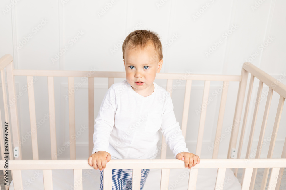 small baby boy 2 years old in the crib looking at the camera in the bright children's room, the child after sleeping small baby boy 2 years old in the crib looking at the camera in the bright children's room, the child after sleeping