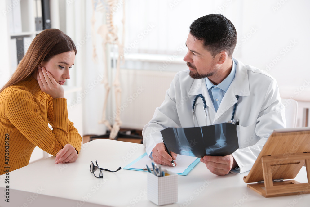 Orthopedist showing X-ray picture to patient at table in clinic Orthopedist showing X-ray picture to patient at table in clinic
