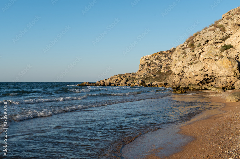 deserted seashore. The water washes over a high rock, and the waves crash on the shore. the golden sandy beach with seashells is illuminated by the rays of the sun at sunset. photowall-paper. 