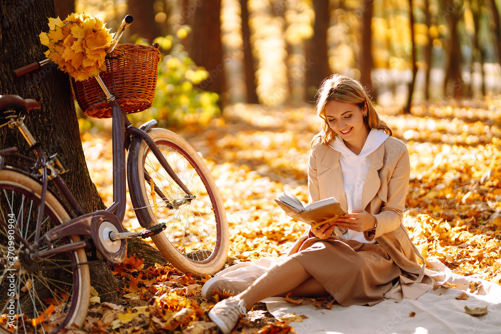 Stylish woman reading a book in the autumn park. Relaxation, enjoying, solitude with nature. - obrazy, fototapety, plakaty 
