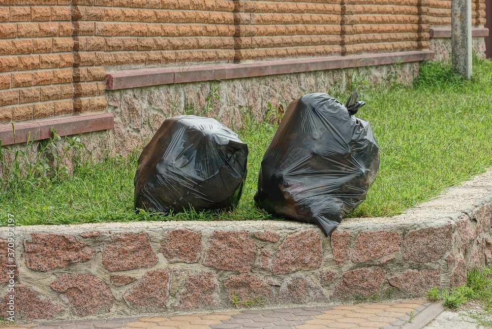 two black plastic bags full of rubbish stand on a brown stone foundation in the green grass outside