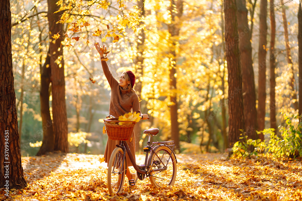 Stylish woman with a bicycle enjoying autumn weather in the park. Beautiful Woman walking  in the autumn forest. - obrazy, fototapety, plakaty 