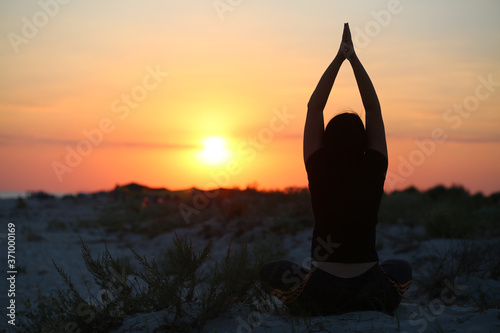 Silhouette of a woman doing yoga at the sunset sea shore