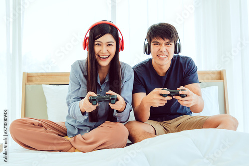 Young Asian Lovely Couple Playing Video Game console on bed in Bedroom. Spends time together. White Background. Male and Female.