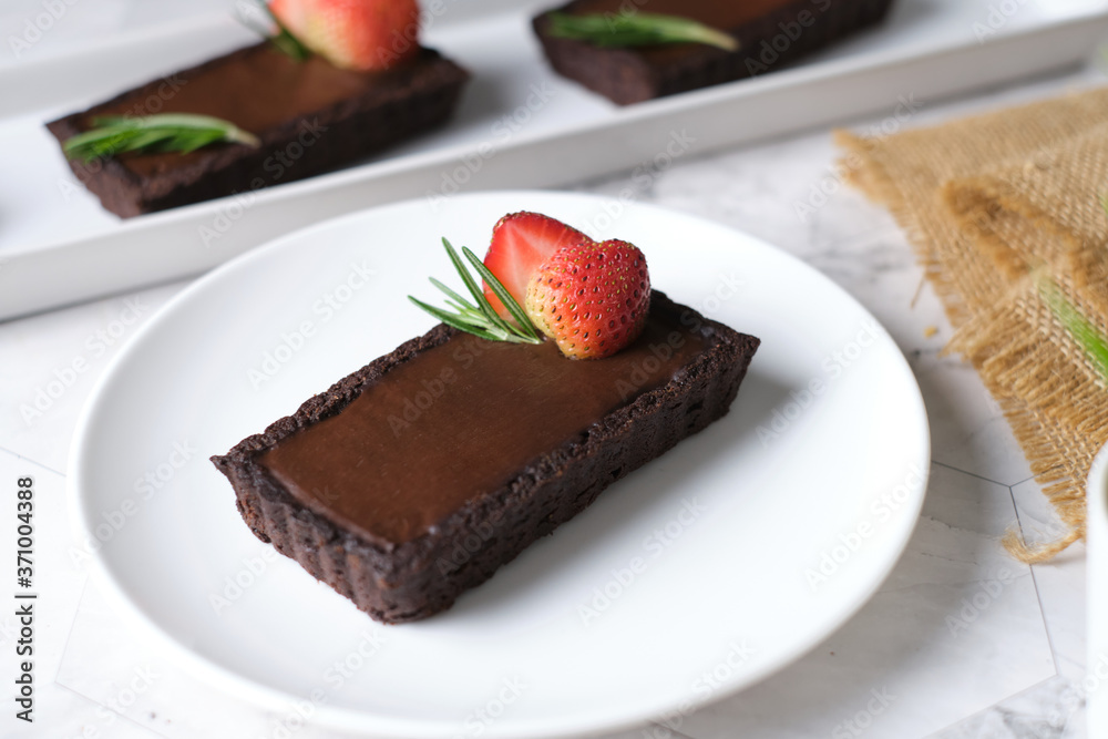 Rectangular chocolate tart with strawberry in white plate set in cafe table. Rectangular chocolate tart with strawberry in white plate set in cafe table.