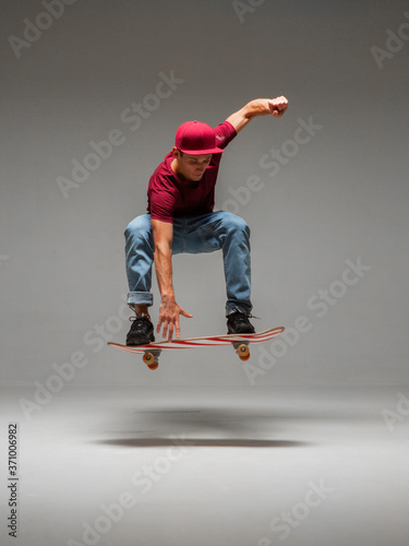 Cool young guy skateboarder levitates on skateboard in studio on grey background. Photography about skateboarding tricks