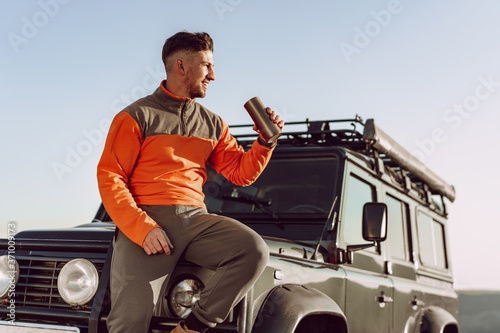 Young man traveler drinking from his thermocup while halt on a hike photo