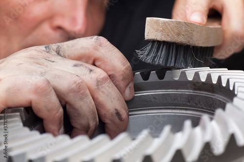 Mechanic with dirty hands cleaning a cog wheel with a steel brush