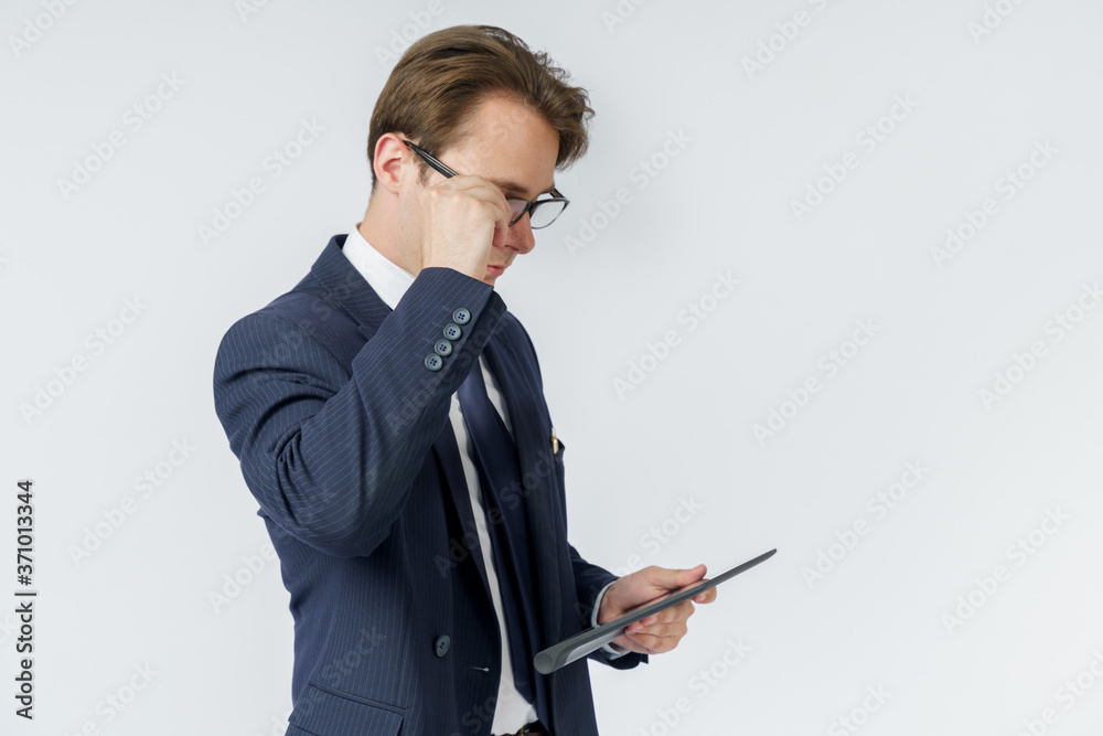 Portrait of a businessman in a blue suit who is holding an electronic tablet in his hands and adjusting his glasses. White background. Portrait of a businessman in a blue suit who is holding an electronic tablet in his hands and adjusting his glasses. White background.