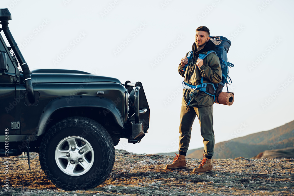 Portrait of a young traveler man in hiking equipment standing near his off-road car Portrait of a young traveler man in hiking equipment standing near his off-road car