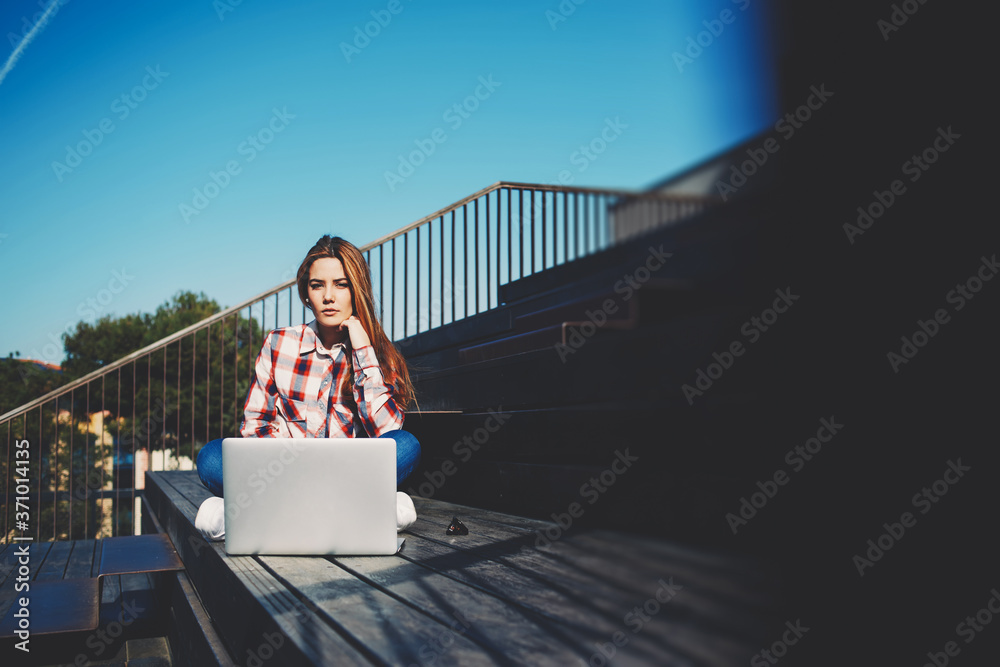 A shot of caucasian college student studying with laptop computer at campus, attractive young woman using laptop sitting on wooden staircase enjoying sunny day outdoors, filtered image