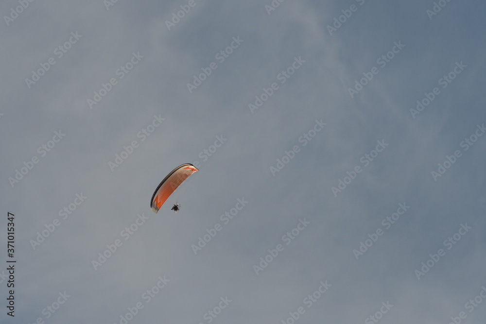 Ein Mann segelt durch die Luft mit seinem hell orangenen Segel. Der Himmel hat sehr dünne Schleier Wolken. Ein Mann segelt durch die Luft mit seinem hell orangenen Segel. Der Himmel hat sehr dünne Schleier Wolken.