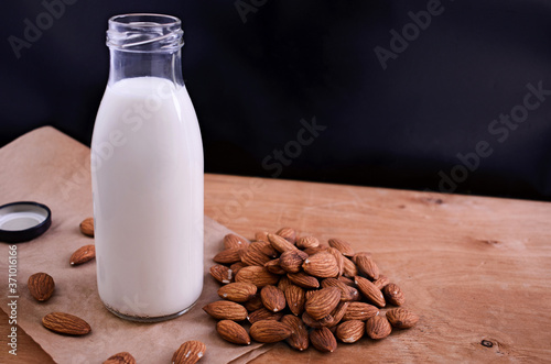 Homemade almond milk in glass bootle with scattered almond on the wooden table. Organic alternative milk. Copy space. Vegan milk from almonds nuts.