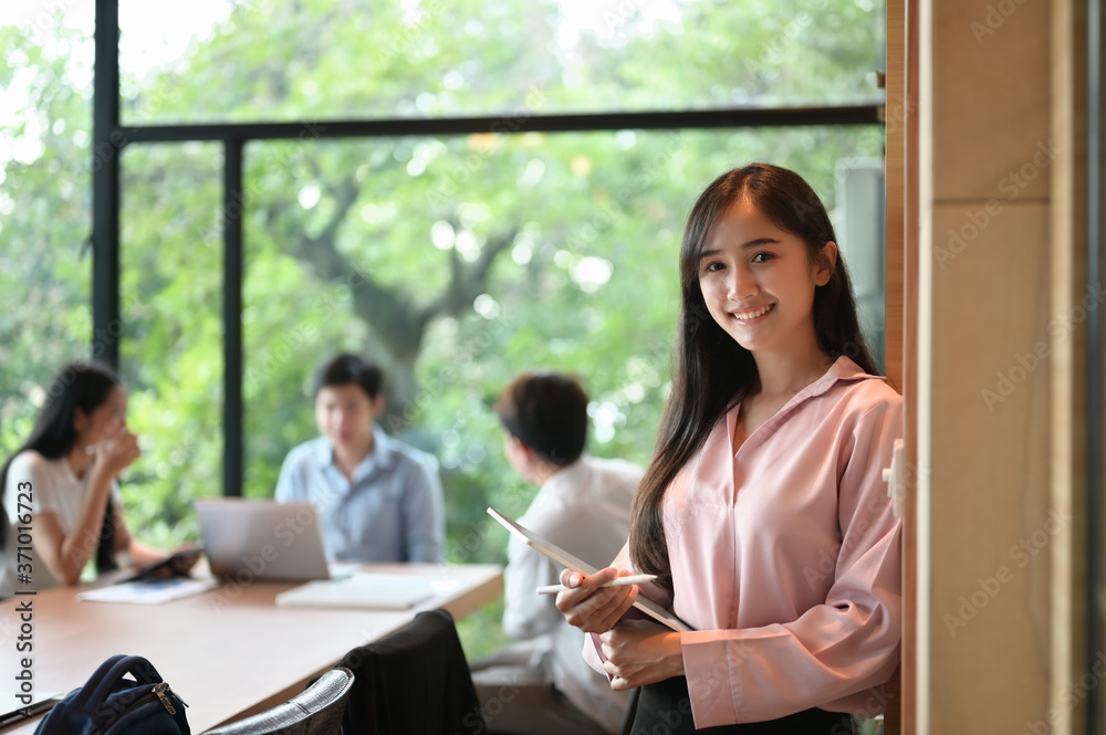 A secretary woman is holding a computer tablet and stylus pen while standing in the meeting room. A secretary woman is holding a computer tablet and stylus pen while standing in the meeting room.