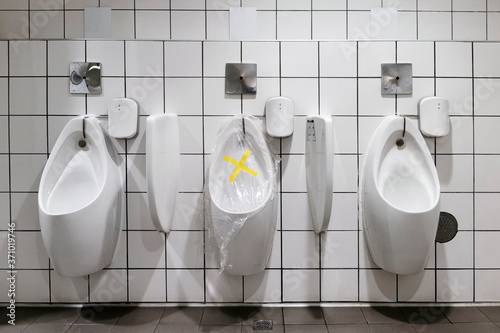 prohibition tape with plastic wrap over urinal in public toilet for people to follow social distancing to avoid infection of coronavirus or covid-19.