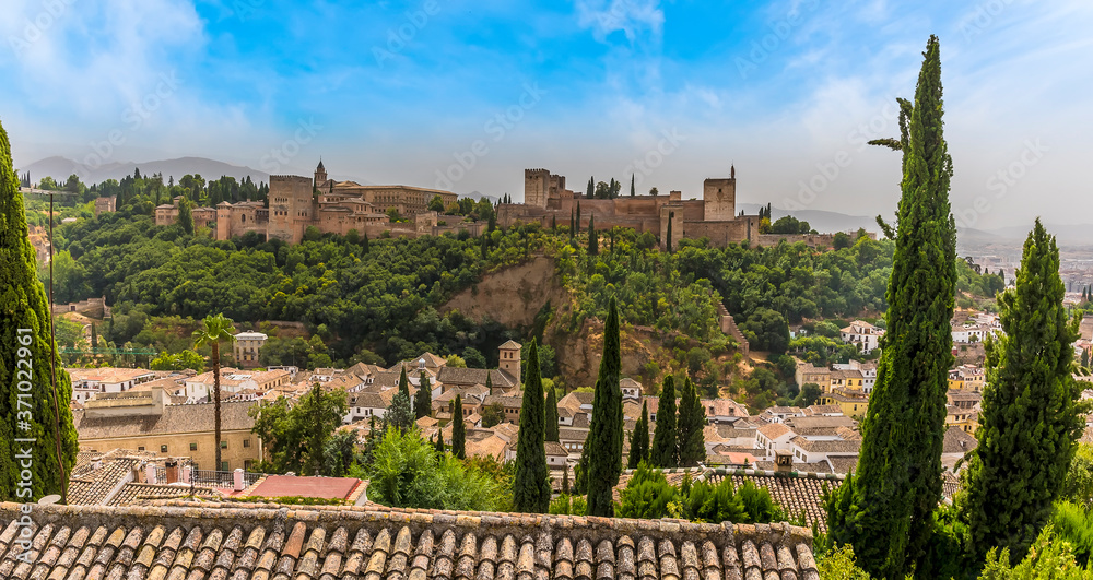 A view from the Saint Nicholas Plaza over the rooftops of the Albaicin district of Granada towards the Alhambra Palace and the Sierra Nevada mountains in the summertime