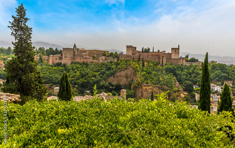A view over the treetops of the Albaicin district of Granada towards the Alhambra Palace and the Sierra Nevada mountains in the summertime