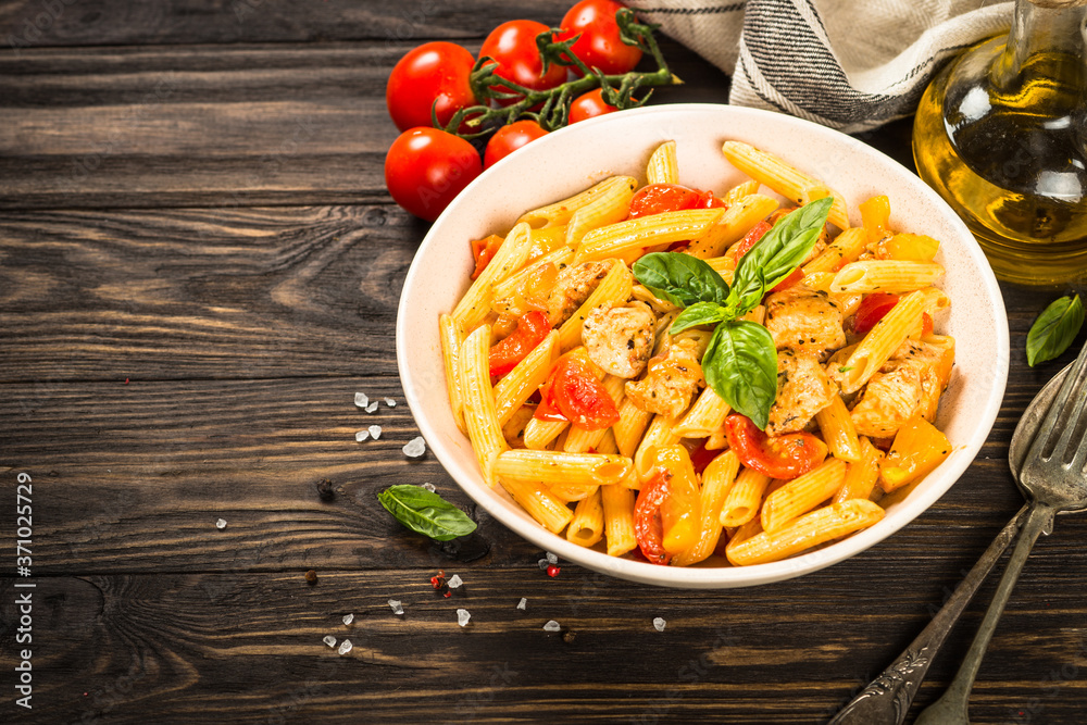 Pasta with chicken and vegetables at wooden table.