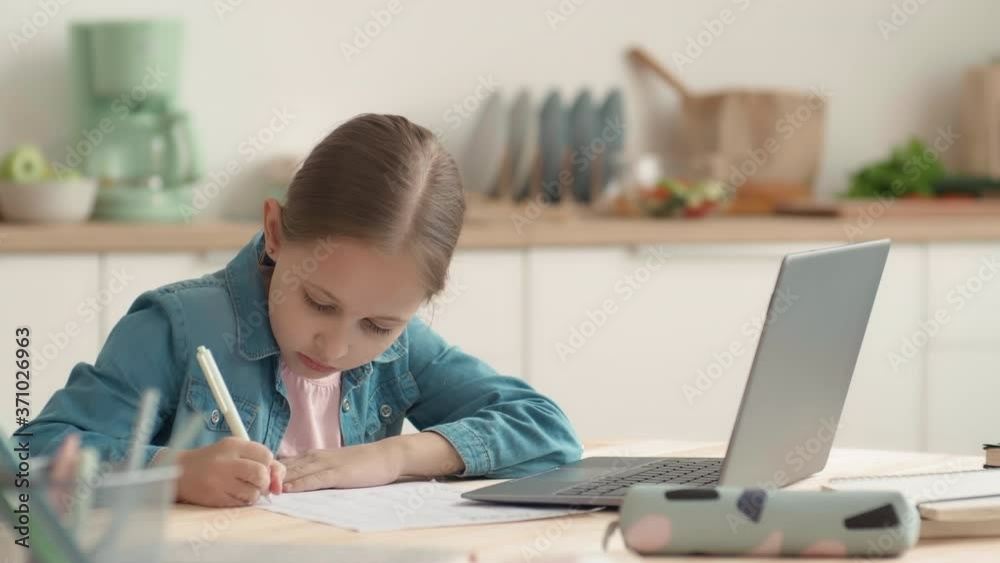 Lockdown of blond-haired Caucasian schoolgirl is sitting at kitchen table, using laptop while doing difficult task Lockdown of blond-haired Caucasian schoolgirl is sitting at kitchen table, using laptop while doing difficult task