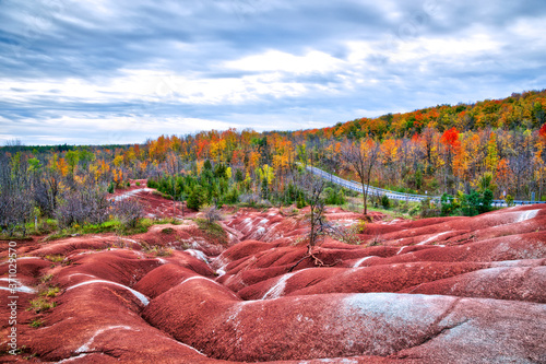 The red and white clay hills of the Cheltenham Badlands formation in Caledon, Ontario, Canada, surrounded by a forest of brightly autumn leaf color... photo
