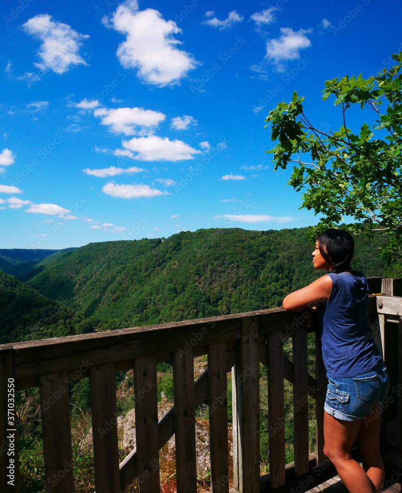 Naklejka premium An Afro-Asian woman seen from behind is admiring the mountain scenery. During the holidays, tourists like to take a break to admire the natural landscape