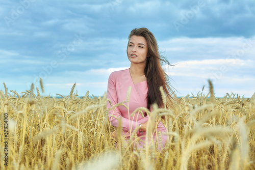 Fototapeta Naklejka Na Ścianę i Meble -  attractive girl stands in a wheat field. against the background of the evening sky