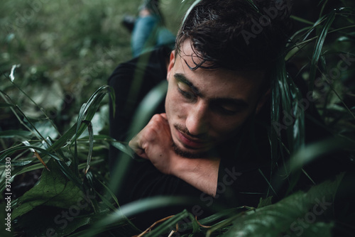 Young man in the forest lying on wet grass and daydreaming while thinking