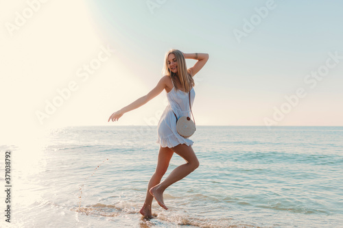 young attractive happy woman dancing turning around by sea beach sunny summer fashion style in white dress vacation