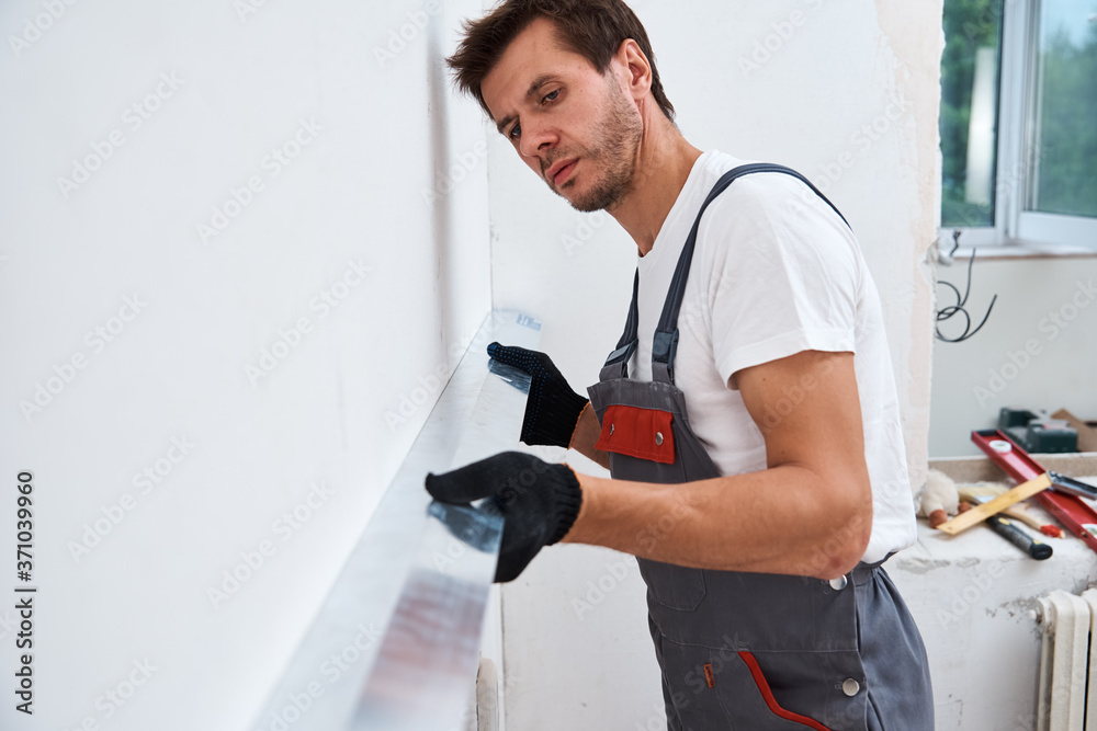 Renovation concept. Male worker plastering a wall using a long spatula Renovation concept. Male worker plastering a wall using a long spatula