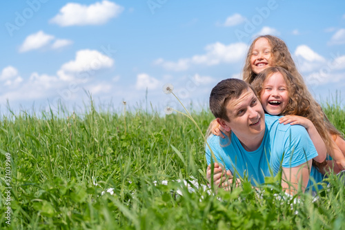Happy father and two little daughters spending time. Dad and daughters playing together on field green grass at summer. Copyspace.