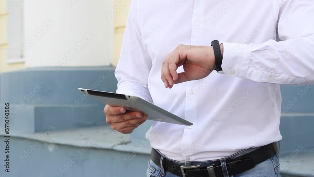 A man in a white shirt and blue jeans raises his hand and looks at the tablett and presses the screen. High quality FullHD footage