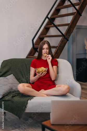 Beautiful domestic girl eating chips, watching tv, sitting at sofa