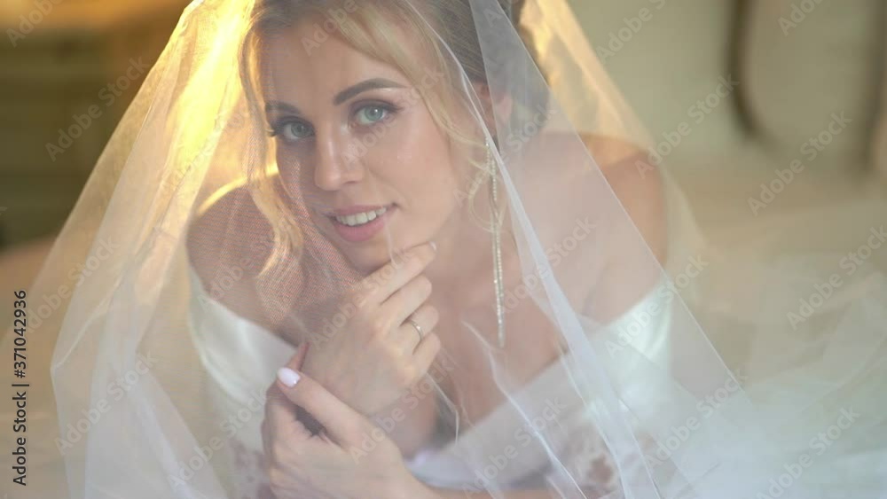 beautiful blonde bride under veil and in a silk robe lying on the bed. beautiful blonde bride under veil and in a silk robe lying on the bed.