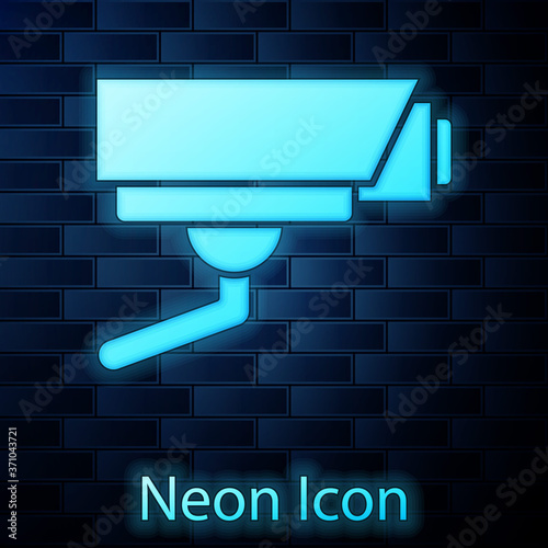 Glowing neon Security camera icon isolated on brick wall background. Vector.