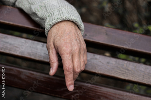 The lonely older hand of a man. An older man sitting on a bench, bokeh background, outdoors