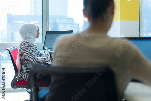 Pretty african muslim business womanand her female american colleague at work sharing office desk with desktops, friendly multiracial coworkers interns having pleasant at workplace together photo