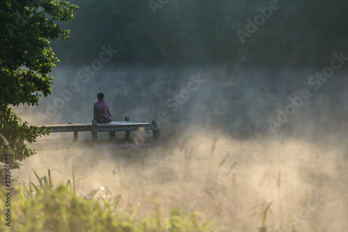 Woman Meditating in solitude on a Dock with morning mist rising from the lake