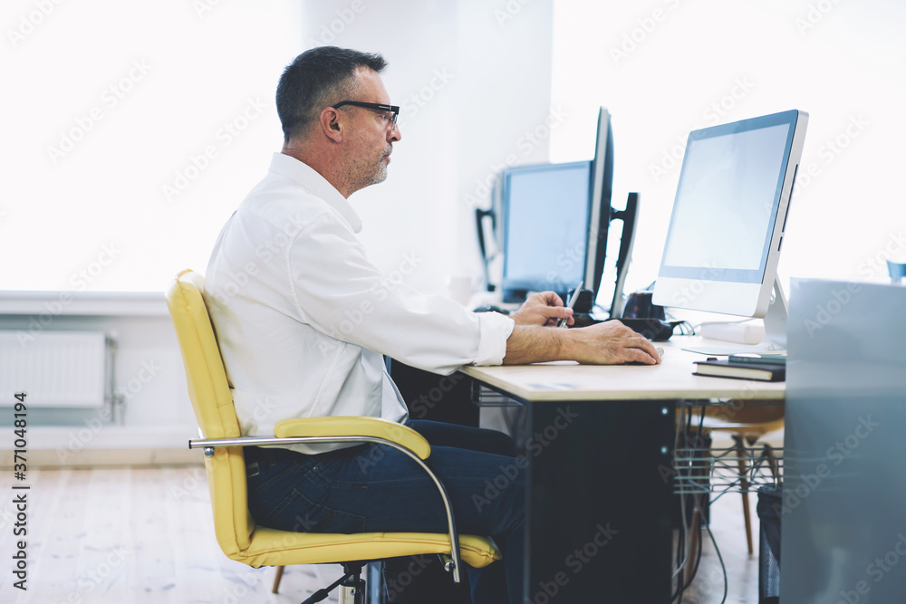 Male employee 50 years old of business company working at modern computer with blank screen for creating new successful presentation surfing on internet websites for searching useful information