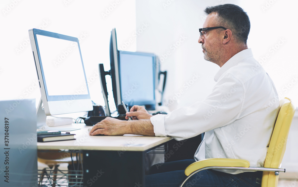 Concentrated mature programmer developing new internet application for high speed transferring money sitting at modern computer during working process.Blank screen for your advertising text message