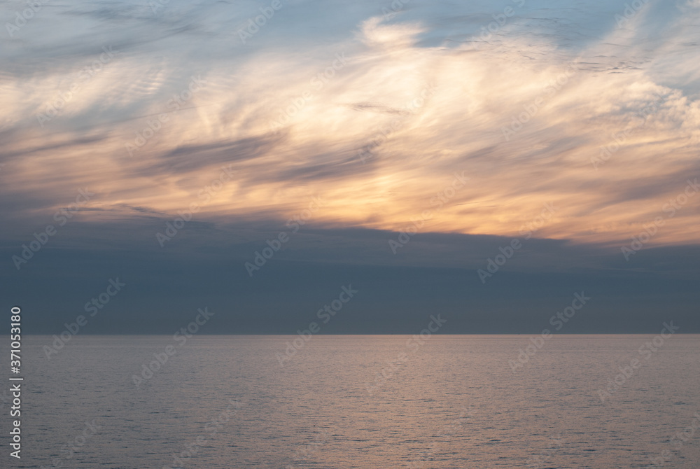 Gray, white and orange clouds on the blue sky above the sea at dawn