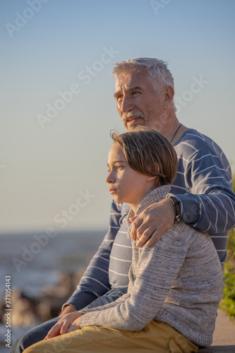boy and grandfather sitting together on the seashore, summer vacation, family traditions