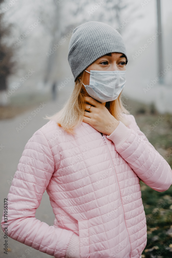 Plakat A young woman is standing near the road in a medical mask.