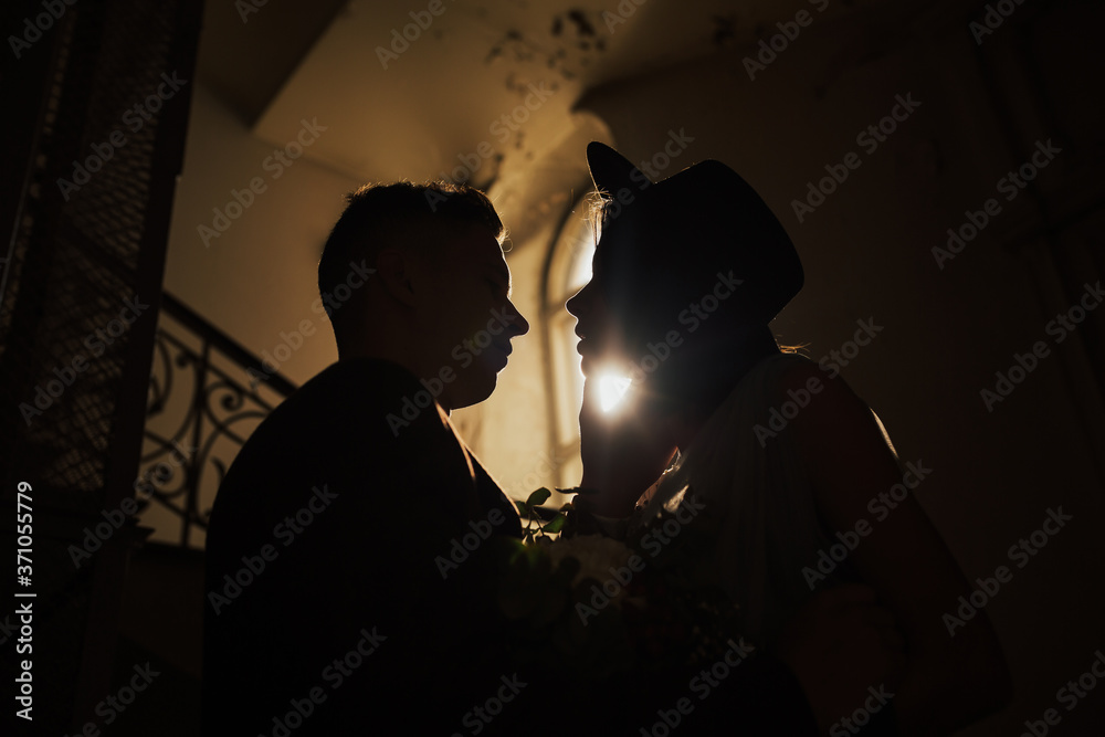 Bride and groom stand near the large window. Close up silhouette of a wedding couple hugging.