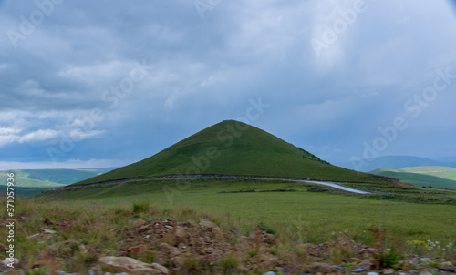 the roadbed is uneven, winding, passes through mountains and cliffs. Clouds are dark, low, with rain. A thick white fog is spreading along the road.