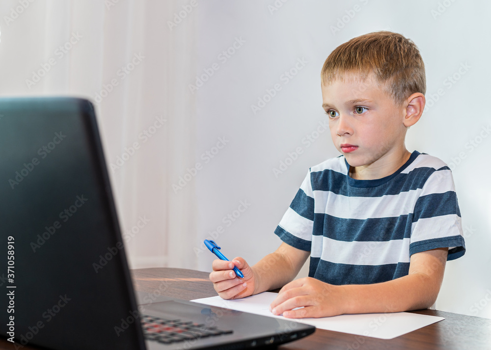 The child looks at the laptop and writes in a notebook. Online learning. Online lessons. The child looks at the laptop and writes in a notebook. Online learning. Online lessons.
