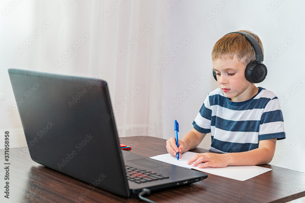 A boy does homework in front of a laptop. Online education.