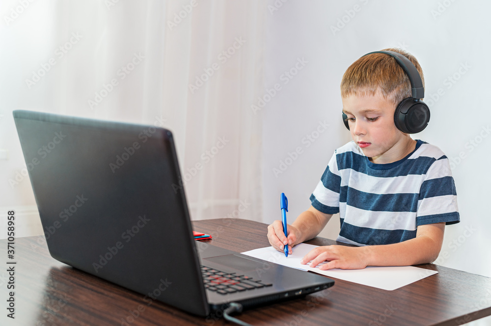 A boy does homework in front of a laptop. Online education. A boy does homework in front of a laptop. Online education.