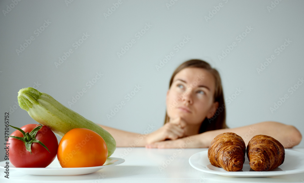 Vegetables and croissants on white table and woman with puzzled sight on background. Balanced diet, healthy nutrition, clean eating or weight loss concept. Banner. Copy space. Vegetables and croissants on white table and woman with puzzled sight on background. Balanced diet, healthy nutrition, clean eating or weight loss concept. Banner. Copy space.