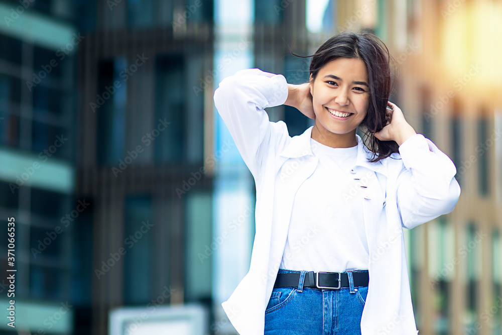 Portrait of Asian attractive woman standing outside. Ethnic happy female, student in white shirt, smiling broadly with show teeth. Positive girl looking at the camera