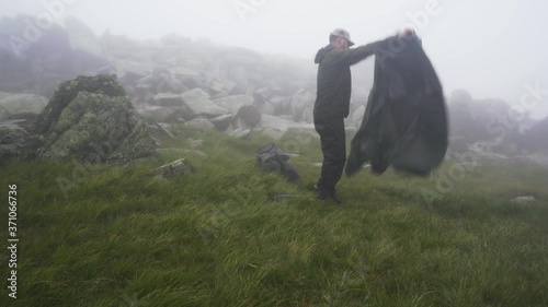 A man setting up a camping tent on a misty windy mountain